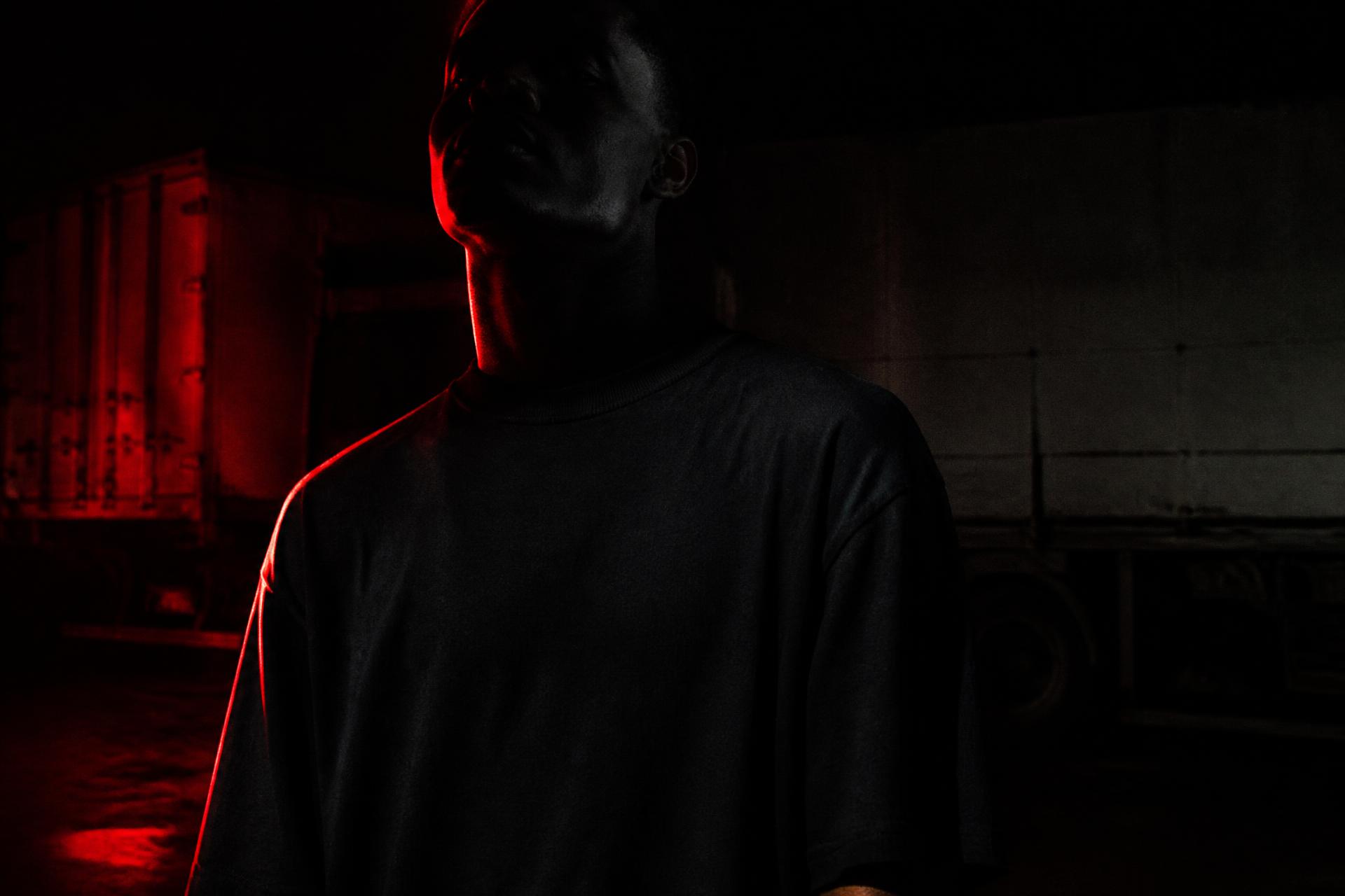 Model in a blacked-out FREIGHTPIMP tee lit by red rim light in a freight yard